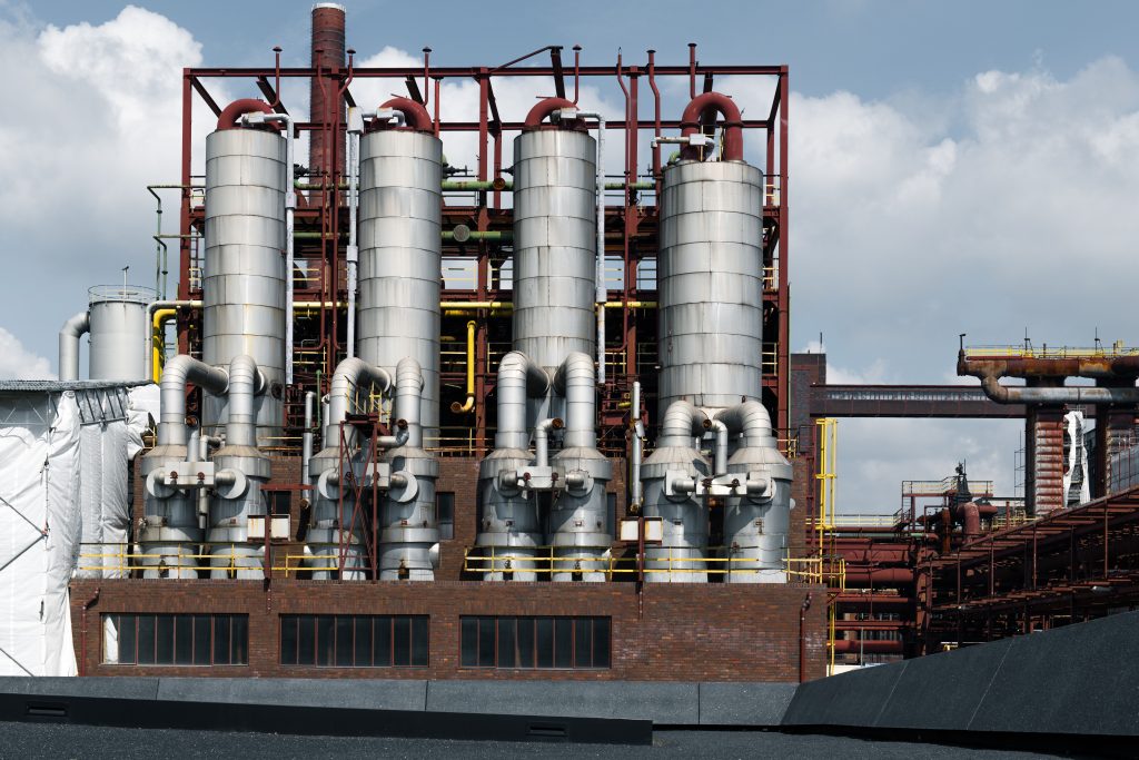 Four tall stainless-steel industrial process vessels connected by piping, valves, and support structures at an industrial facility.